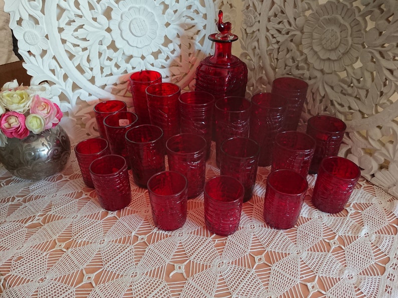 May include: A set of 15 red glass tumblers and a matching decanter with a stopper. The glasses and decanter have a textured, embossed design.