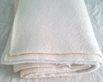 May include: A white fleece blanket folded on a white surface with a floral pattern. The blanket has a stitched edge.