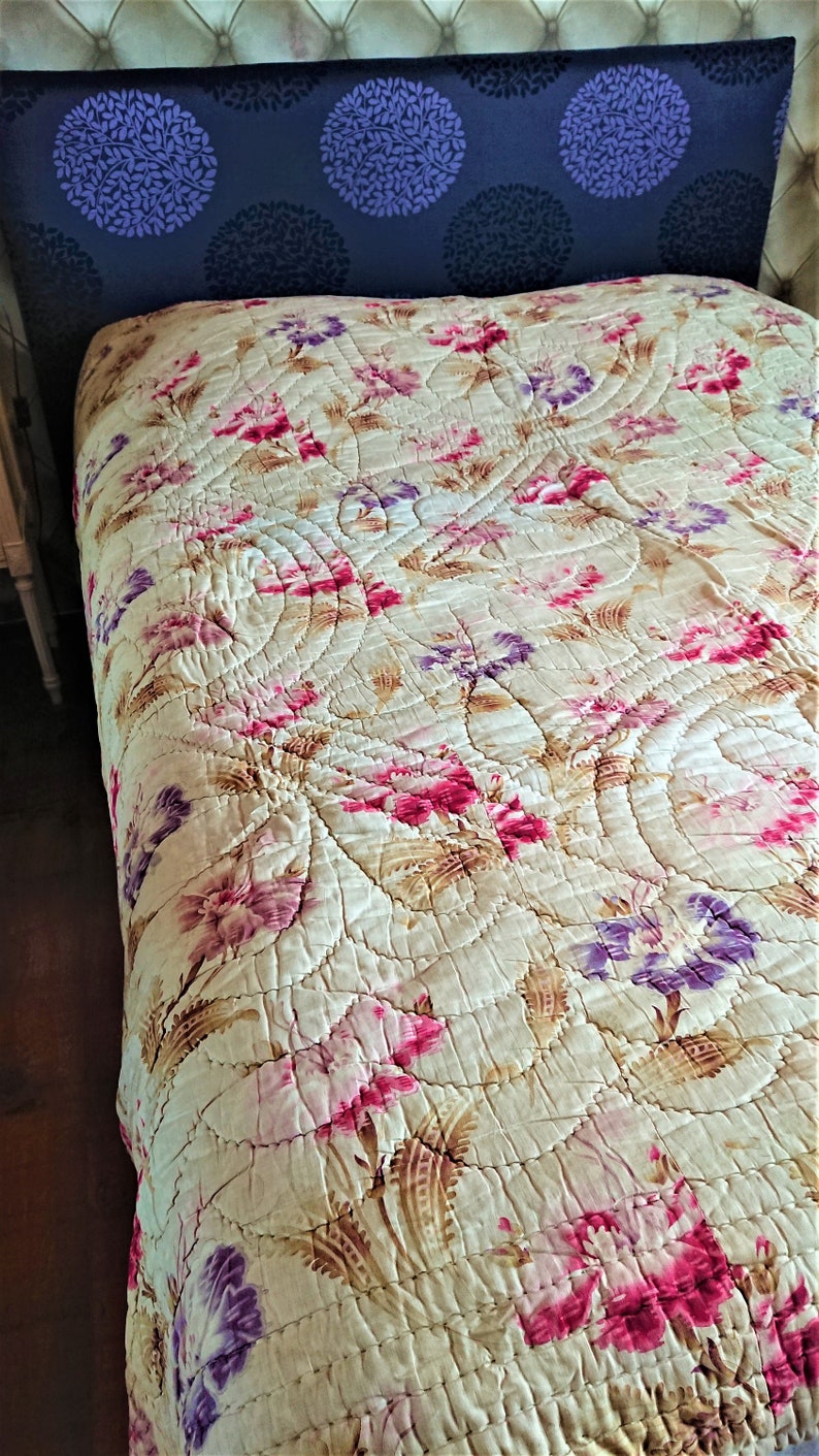 May include: A vintage floral quilt with a cream background and pink, purple, and brown floral patterns. The quilt is quilted in a circular pattern.