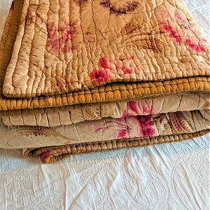 May include: A folded floral patterned quilt with a brown border. The quilt is made of a soft, lightweight fabric and has a vintage look.