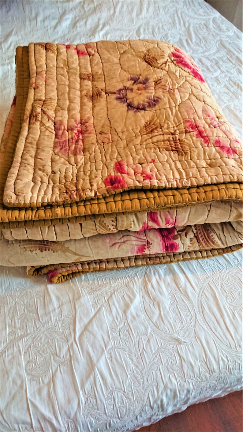 May include: A folded floral patterned quilt with a brown border. The quilt is made of a soft, lightweight fabric and has a vintage look.