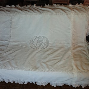 May include: White lace bedspread featuring a delicate embroidered design of two children playing within a circular frame. The bedspread has a scalloped edge and is crafted from a soft, lightweight fabric.