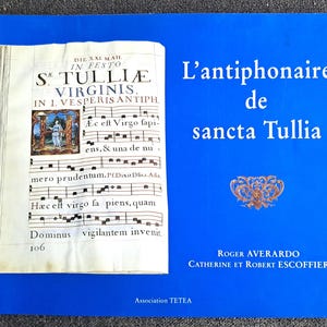 May include: A blue book cover with the title "L'antiphonaire de sancta Tullia" and the author's names "Roger Averardo, Catherine et Robert Escoffier". The cover features a page from an old book with musical notation and a small illustration.