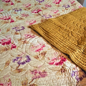 May include: A vintage floral quilt with a yellow quilted throw on top. The quilt features a floral pattern with pink, purple, and white flowers on a cream background.