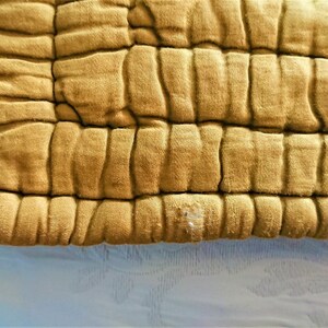 May include: Close-up of a mustard yellow quilted fabric with a textured surface. The fabric has a slightly worn appearance.