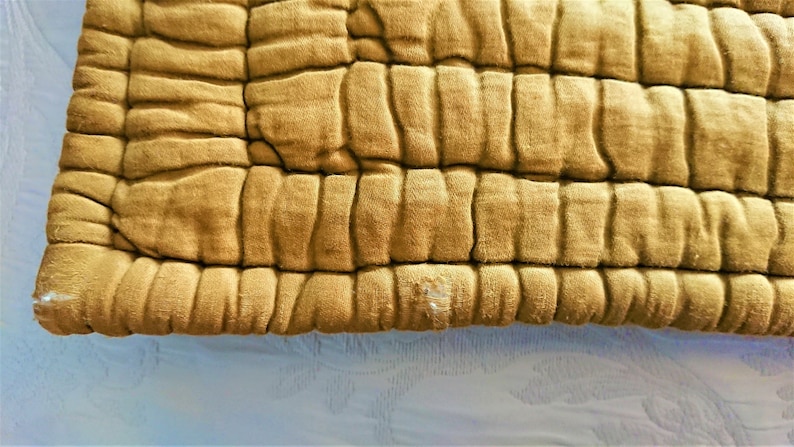 May include: Close-up of a mustard yellow quilted fabric with a textured surface. The fabric has a slightly worn appearance.
