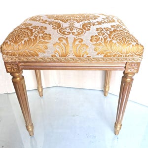May include: A gold-painted wooden stool with a gold and white patterned fabric seat.