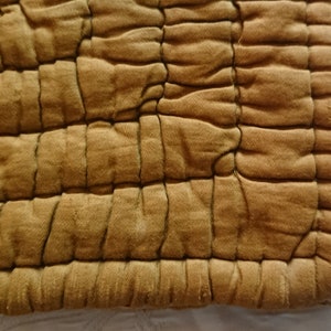 May include: A close-up of a mustard yellow quilted fabric with a square pattern. The fabric is soft and textured.