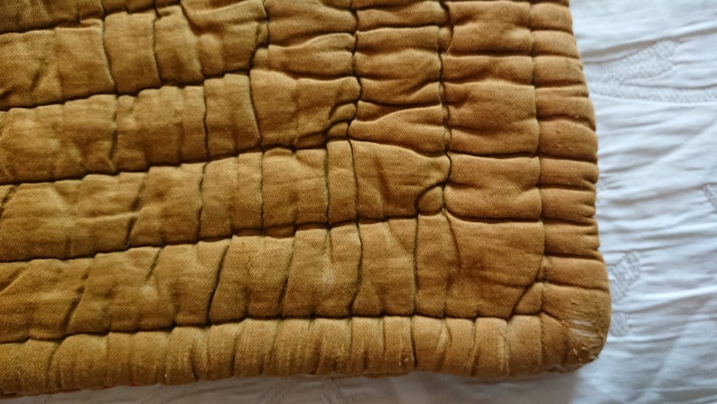 May include: A close-up of a mustard yellow quilted fabric with a square pattern. The fabric is soft and textured.