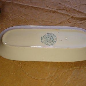 May include: A white oval ceramic dish with a green and white seal on the bottom. The seal reads "Fabrique en France" and "J. & H. NOULLIER, PARIS".