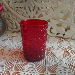 May include: A red glass tumbler with a textured pattern. The tumbler is sitting on a white crocheted tablecloth.