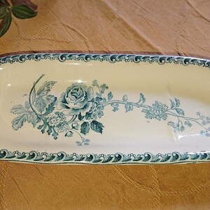 May include: An oval ceramic dish with a blue and white floral design. The dish has a raised edge and a scalloped rim.