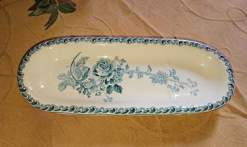 May include: An oval ceramic dish with a blue and white floral design. The dish has a raised edge and a scalloped rim.