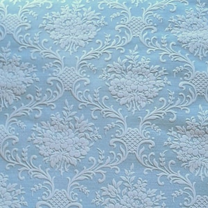 Könnte beinhalten: Eine hellblaue Tapete mit einem weißen, geprägten Blumenmuster. Das Muster zeigt ein sich wiederholendes Design aus stilisierten Blumen und Blättern.