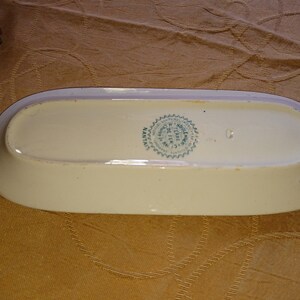 May include: A white oval ceramic serving dish with a green and white circular stamp on the bottom. The stamp reads "MADE IN HOLLAND BY TERRA SIGILLATA"