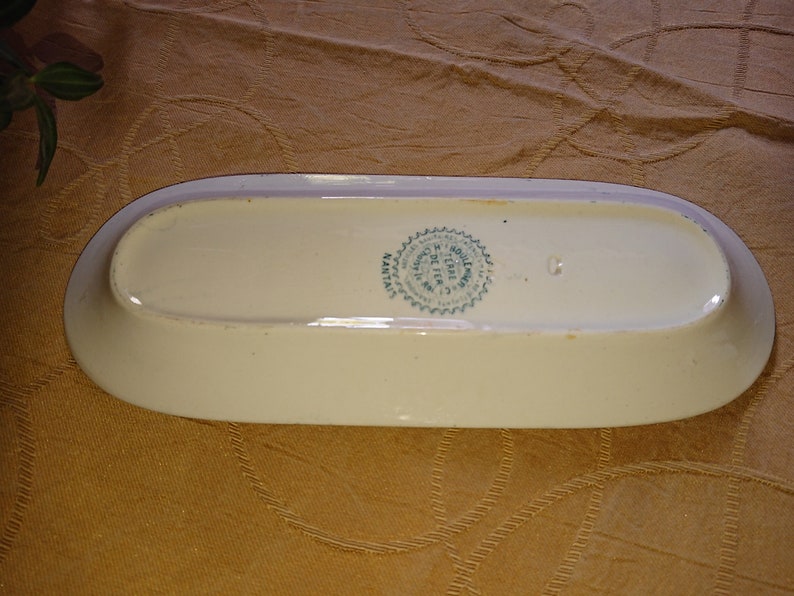 May include: A white oval ceramic serving dish with a green and white circular stamp on the bottom. The stamp reads "MADE IN HOLLAND BY TERRA SIGILLATA"