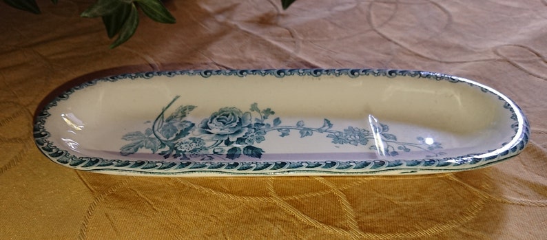 May include: An oval ceramic dish with a blue and white floral design. The dish has a raised rim and a divided interior.