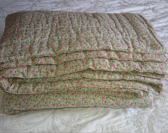 May include: A folded green quilted blanket with a floral pattern featuring small pink and orange flowers.