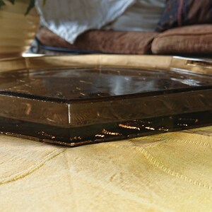 May include: A clear glass octagonal tray with a brown tint. The tray is sitting on a beige fabric surface.