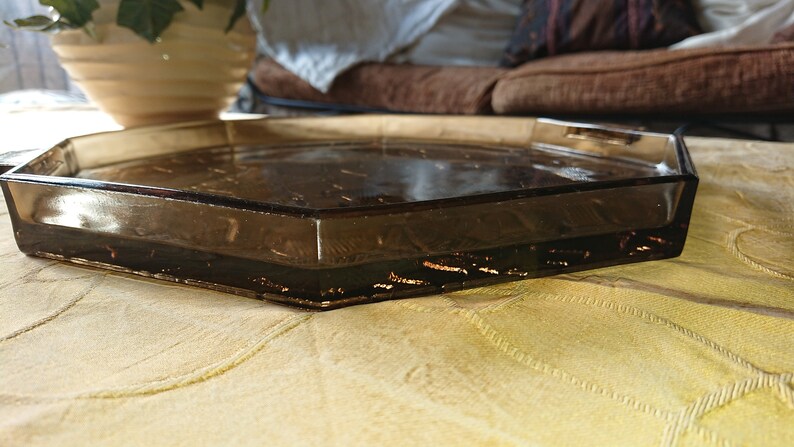 May include: A clear glass octagonal tray with a brown tint. The tray is sitting on a beige fabric surface.