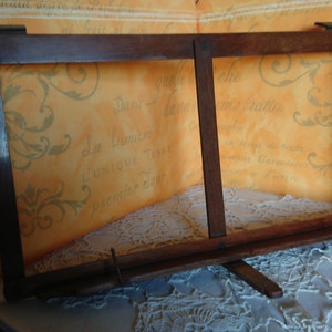 May include: A wooden book stand with two adjustable panels. The stand is made of dark brown wood and has a simple design. It is sitting on a white lace tablecloth.