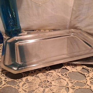 May include: Two silver serving trays with a slightly raised edge and a polished finish. The trays are stacked on top of each other.