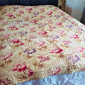 May include: A vintage floral quilt with a cream background and pink, purple, and brown flowers. The quilt is quilted in a pattern of curved lines.