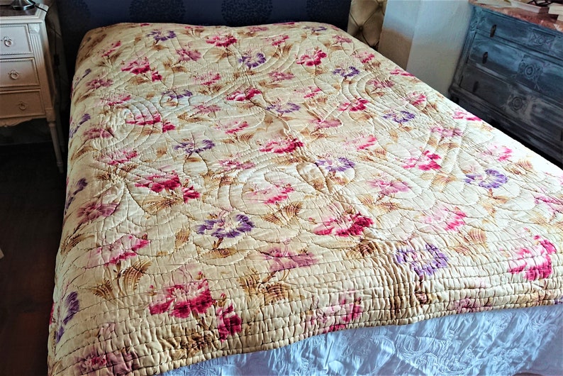 May include: A vintage floral quilt with a cream background and pink, purple, and brown flowers. The quilt is quilted in a pattern of curved lines.