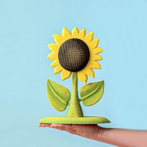 Handcrafted Montessori-approved sunflower toy made of wood, balancing on a hand against a turquoise background