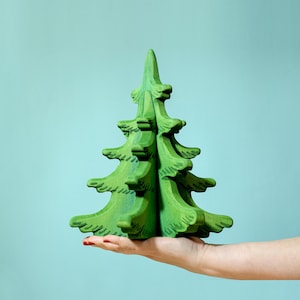 May include: A hand holds a green wooden Christmas tree ornament. The tree is made of multiple pieces that fit together to create a 3D shape.