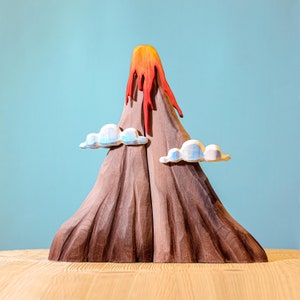 Handcrafted wooden volcano toy with vibrant red and orange lava flowing down, complemented by whimsical blue and white clouds, against a soft blue background.