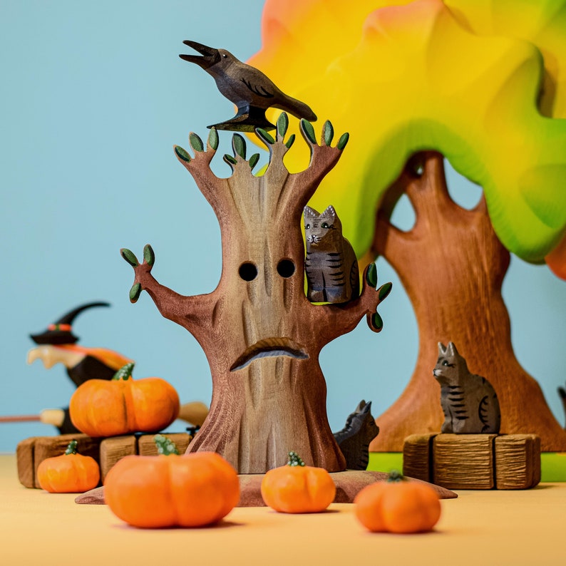 A hand-carved wooden tree figurine with a bat accessory, surrounded by miniature pumpkins, ghost, and stone toys on a wooden surface.