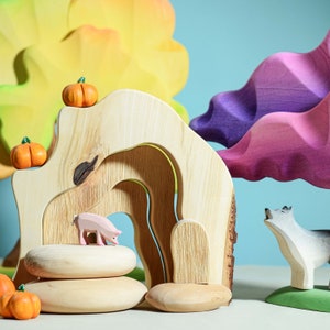 Wooden scene with a pig figurine inside a natural wood arch, with a wolf outside, surrounded by colorful trees and pumpkins.