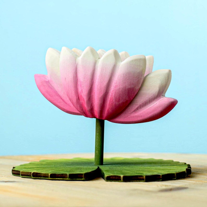 A beautifully crafted wooden lotus with delicate shading on its petals, presented on a wooden table with a soft blue backdrop.