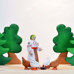 A vibrant wooden toy setup featuring a painted figure in traditional attire with two hens, against a background of green trees on a wooden surface.