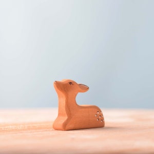 A small wooden figurine of a deer, a unique handmade gift, sits gracefully on a wooden surface against a soft blue background.