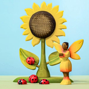 Handcrafted sunflower toy with ladybug figurines and a wooden fairy, promoting imaginative Waldorf playtime