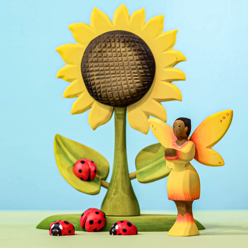 Handcrafted sunflower toy with ladybug figurines and a wooden fairy, promoting imaginative Waldorf playtime