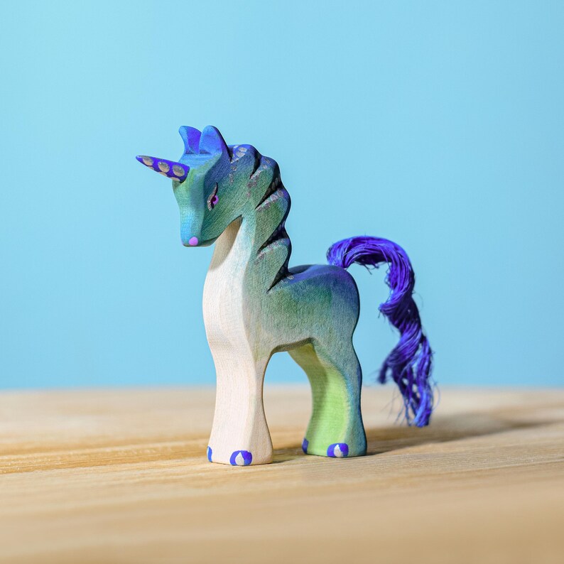 Wooden unicorn toy with a purple tail, sitting on a wooden table.