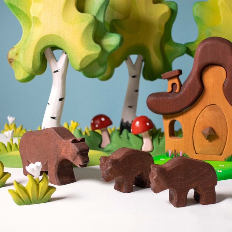 A playful wooden forest scene with bears, birch trees, a mushroom, and a small house, all set on a green base.