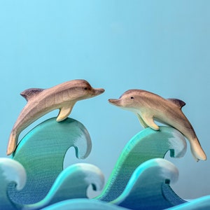 Two wooden dolphins leap side by side over rolling blue waves, an image capturing the joy of play and the essence of ocean life, brought to life by BumbuToys’ skilled artisans.