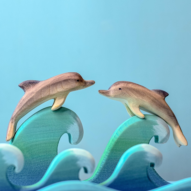 Two wooden dolphins leap side by side over rolling blue waves, an image capturing the joy of play and the essence of ocean life, brought to life by BumbuToys’ skilled artisans.