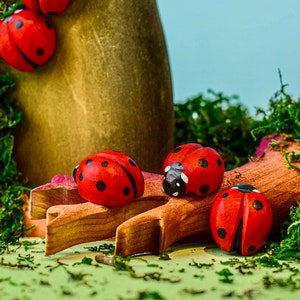 A collection of wooden ladybug toys scattered on a fallen log surrounded by green moss, evoking a forest scene.