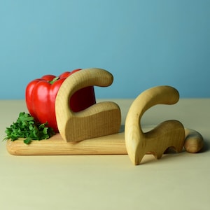 May include: Two wooden kitchen tools shaped like a C on a wooden cutting board with a red bell pepper and green parsley.