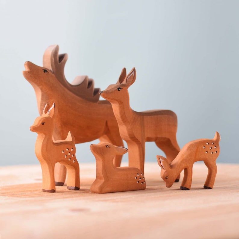 A family of wooden deer toys with detailed carvings and spots, positioned on a wooden surface against a soft gray background.