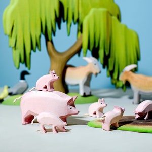 Set of wooden farm animals including goats and pigs under a felt tree, Waldorf-style educational set.