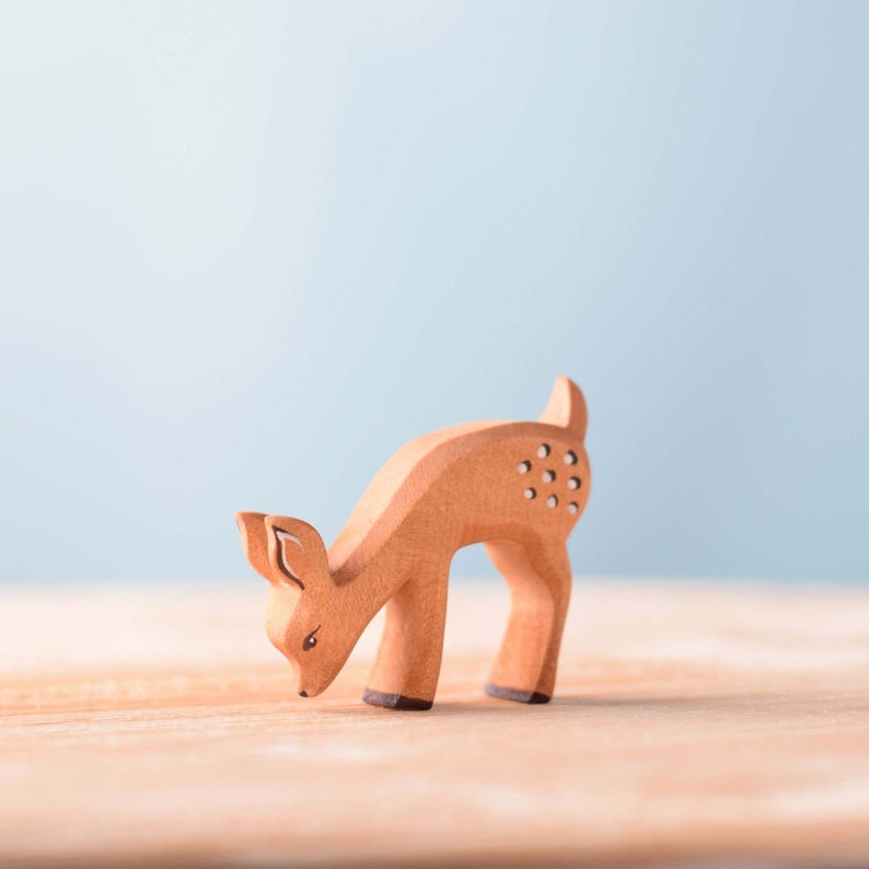 A wooden deer figurine standing on a smooth surface against a soft blue background, representing a unique handmade gift.