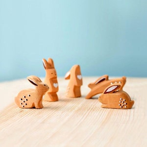 A group of charming wooden rabbit figurines in various playful positions on a wooden surface against a pastel blue background, each meticulously crafted as a unique handmade gift.