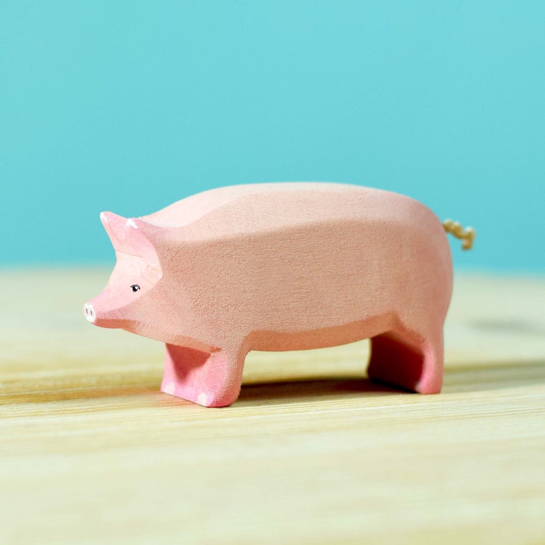 A solitary large wooden pig figure standing on a wooden surface, painted in pastel pink, with a visible grain texture.