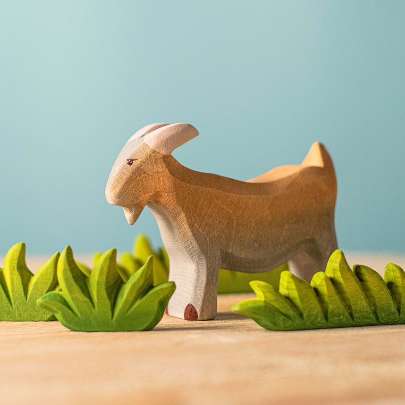 Wooden goat toy amidst green felt leaves, a Montessori-inspired play scene.